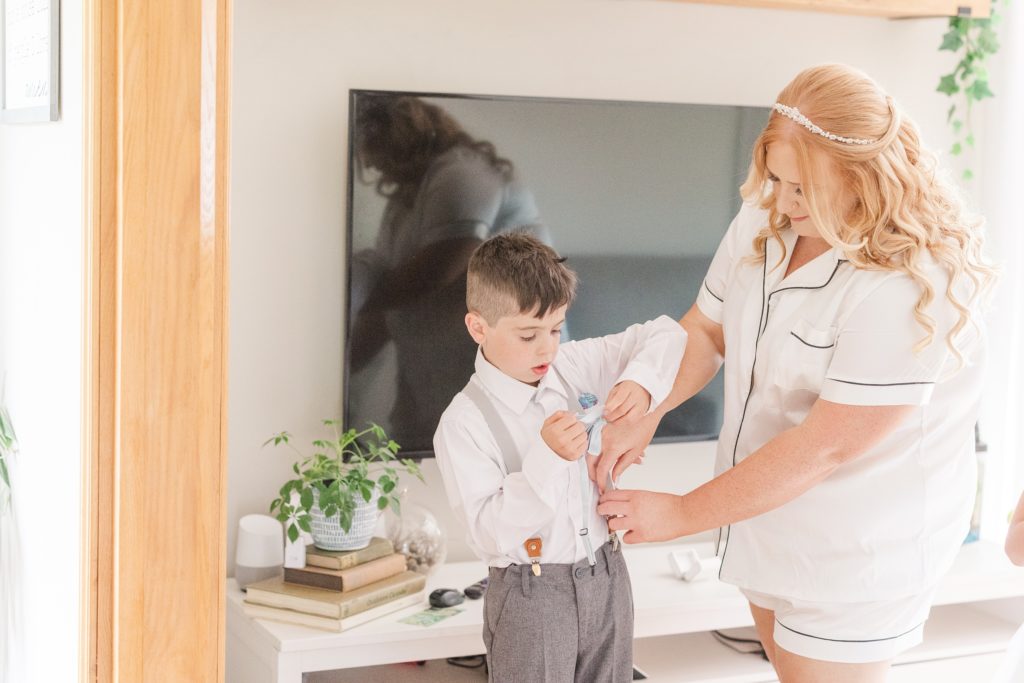 aiden laurette photography | red headed women dressed in white short sleeve top and shorts helps boy in formal dress do up his suspenders