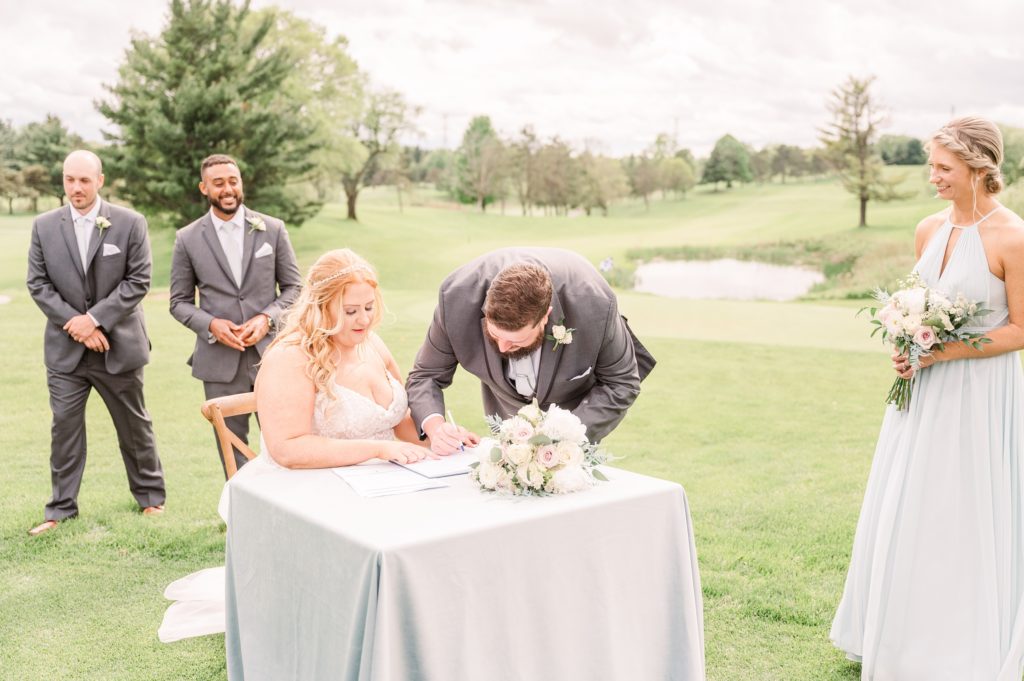 aiden laurette photography | bride and groom sitting at table signing paper while maid of honor and groomsmen look on