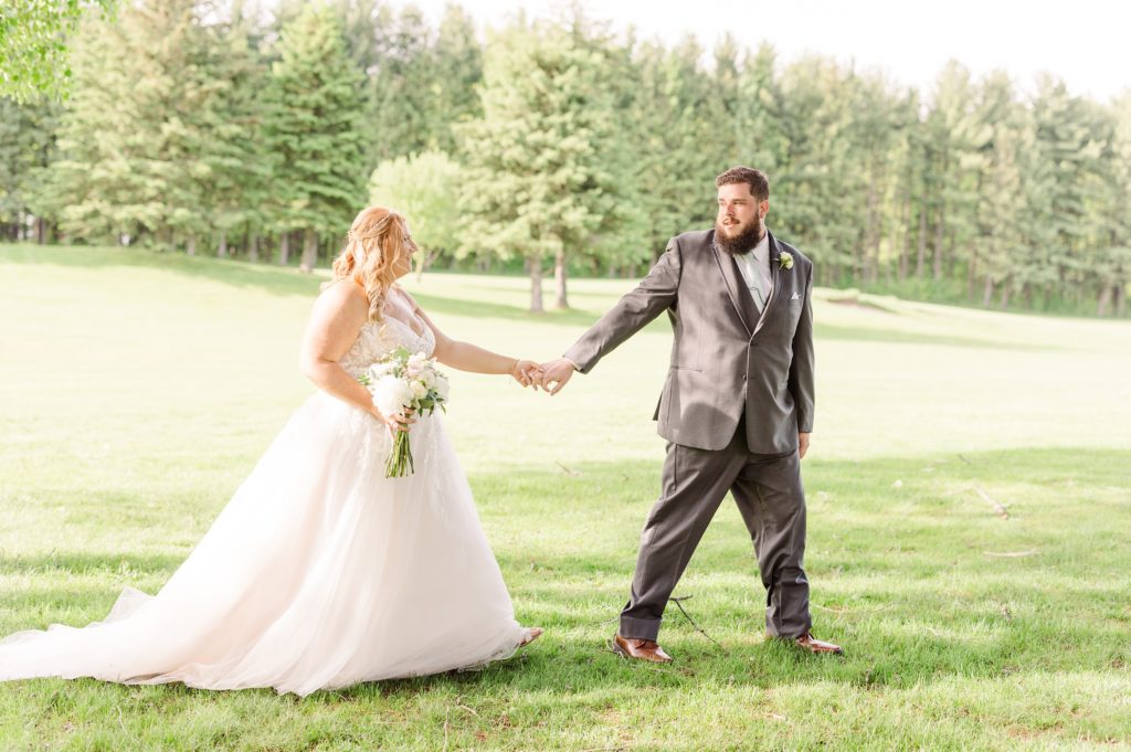 aiden laurette photography | bride and groom pose on grass in front of trees holding hands and walking