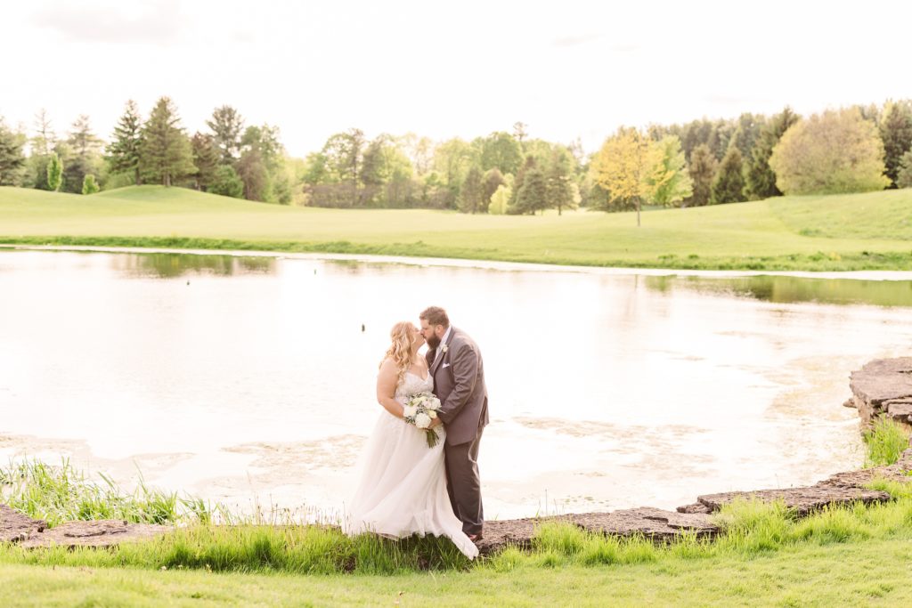 aiden laurette photography | bride and groom pose on grass in front of trees and lake