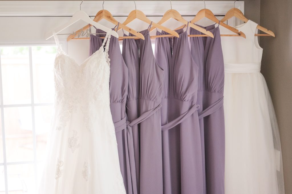 Aiden Laurette Photography | Wedding gown hangs up next to purple bridesmaids dresses and white flower girl dress