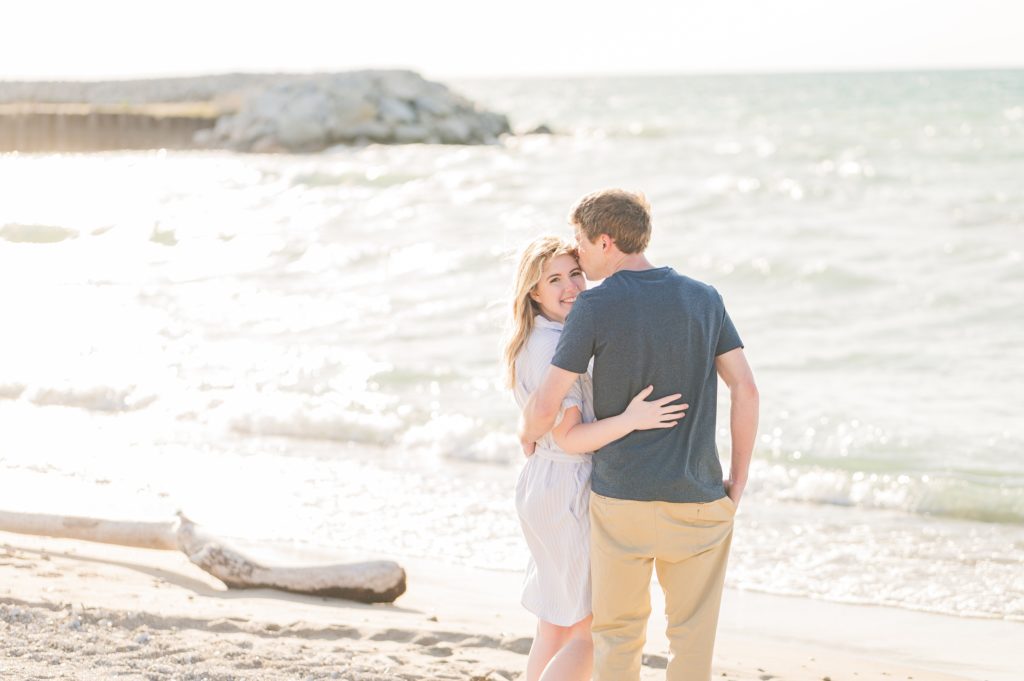 Aiden Laurette Photography | Preparing for an Engagement Session | man and woman stand on beach, woman looks at camera smiling while man kisses her forehead