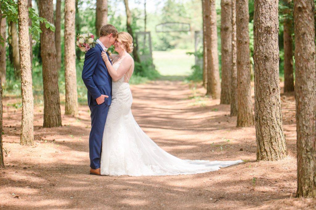Aiden Laurette Photography | bride in white dress and groom in blue suit embrace in front of trees