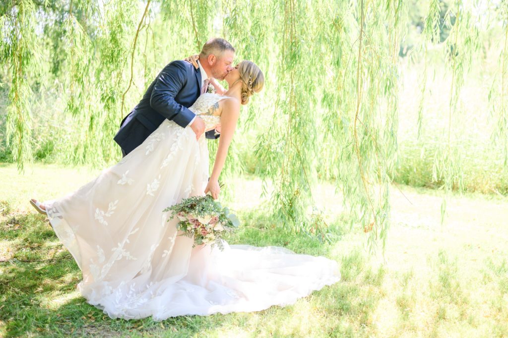 Aiden Laurette Photography | bride and groom kiss in field under willow tree
