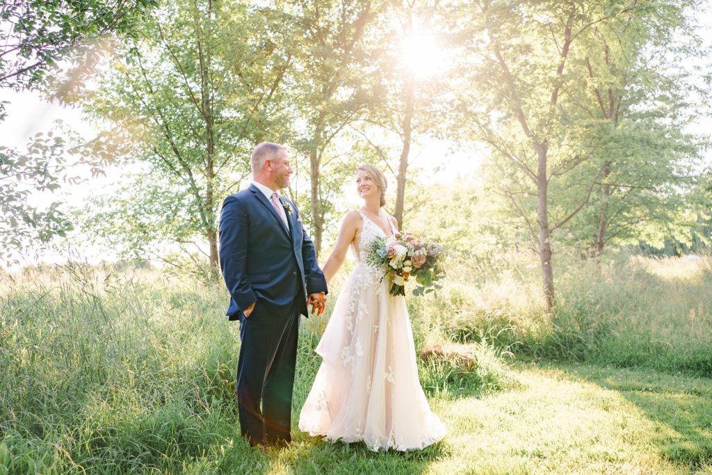Aiden Laurette Photography | bride and groom hold hands in front of willow trees in field