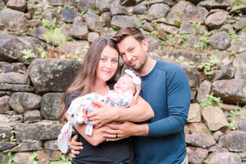 Aiden Laurette Photography | man and woman pose with their newborn in front of rock wall