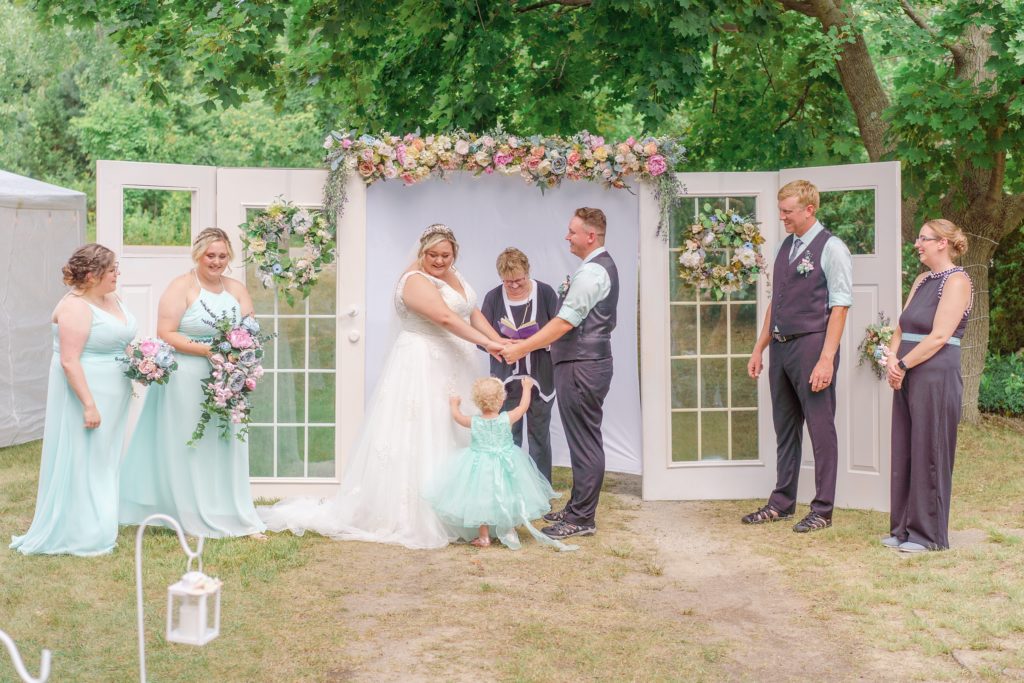Aiden Laurette Photography | bride and groom stand at alter with wedding party on either side and daughter in mint green dress in front of them