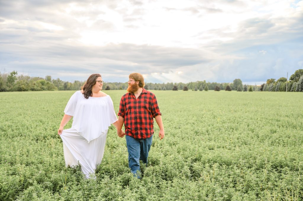 Aiden Laurette Photography | Woman in white dress and man in plaid shirt walk in field