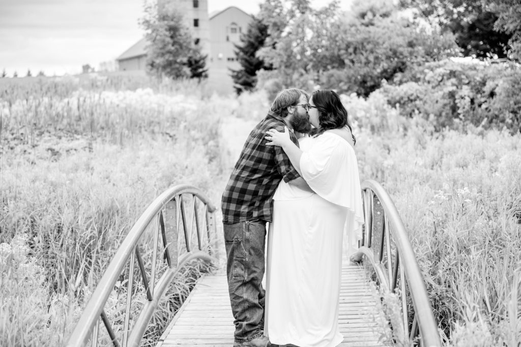 Aiden Laurette Photography | Woman in white dress and man in plaid shirt kiss on bridge