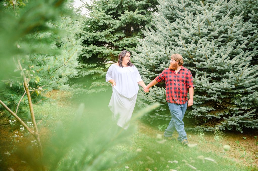 Aiden Laurette Photography | Woman in white dress and man in plaid shirt walk near evergreen trees